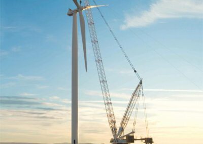 A crane lifts a wind turbine on a dirt field, showcasing the construction of renewable energy infrastructure.